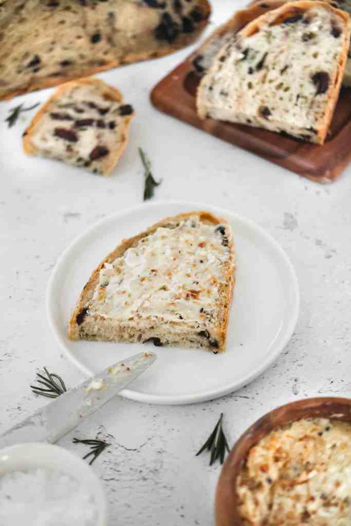 A slice of rosemary olive no knead bread on a plate with butter
